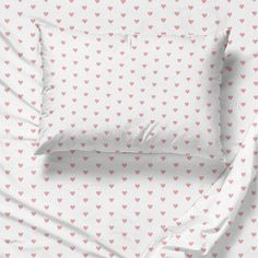 a bed with pink hearts on it and two pillows next to each other in front of a white background