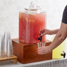 a person is holding a glass in front of a large jug filled with water and ice