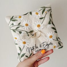 a hand holding a ring pillow that has daisies on it with the words, not to & fro