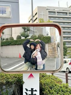 a man and woman taking a selfie in the reflection of a mirror on a street