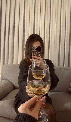 a woman taking a selfie with two wine glasses in front of her and the other hand holding a cell phone