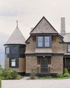 a large brown house with two towers on the front and second story, surrounded by greenery