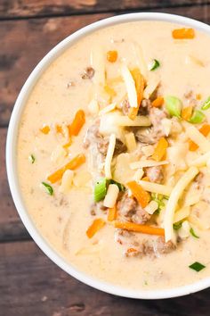 a white bowl filled with soup and cheese on top of a wooden table next to a spoon