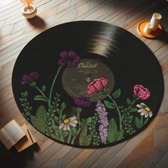 a record with flowers painted on it sitting on the floor in front of a vase