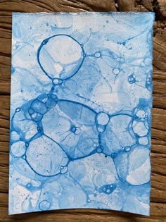 a piece of paper with blue and white paint on it sitting on top of a wooden table