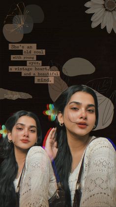 two young women sitting next to each other in front of a wall with flowers on it