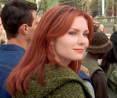 a woman with long red hair standing in front of other people and looking off into the distance