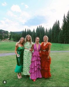 three women standing next to each other on a lush green field with trees in the background