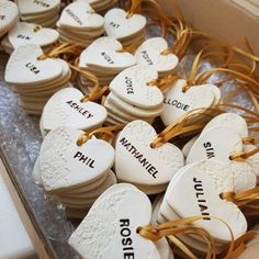 some white heart shaped cookies with names on them in a cardboard box, tied with twine