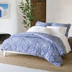 a bed with blue and white comforter in a bedroom next to a plant on the floor