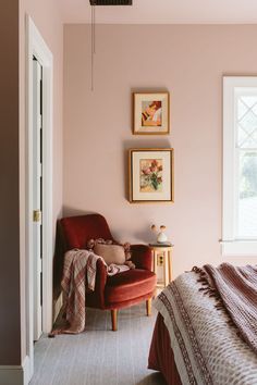 a bedroom with pink walls and pictures on the wall above the bed, along with a red chair