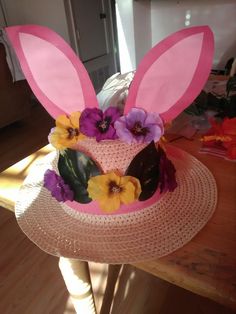 a pink hat with purple and yellow flowers on it sitting on top of a wooden table