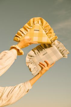 a woman holding up a yellow pillow in front of her face with the sky behind her