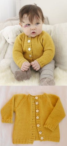 a baby wearing a yellow cardigan sitting on top of a white bed next to a stuffed animal