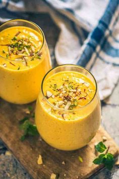 two glasses filled with yellow liquid sitting on top of a wooden cutting board next to each other