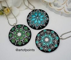 three pendants with blue and green designs are on a white table next to flowers