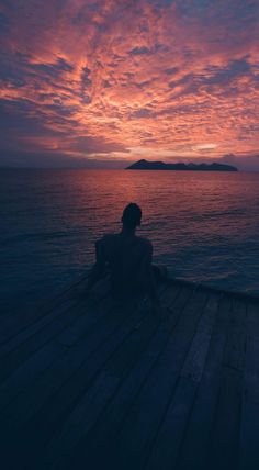 a person sitting on a dock watching the sunset