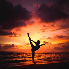 a woman is doing yoga on the beach at sunset with her arms in the air