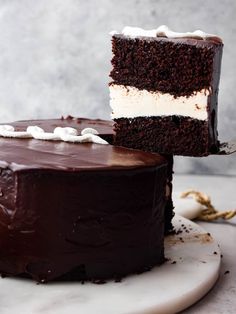 a piece of chocolate cake with white frosting on a plate next to the rest of the cake