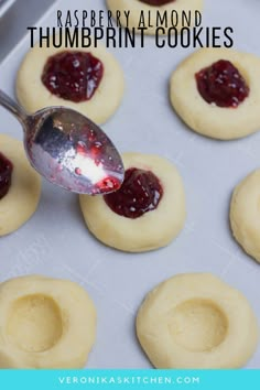 a spoon is being used to scoop jam onto cookies on a baking sheet with the words raspberry almond thumbprint cookies