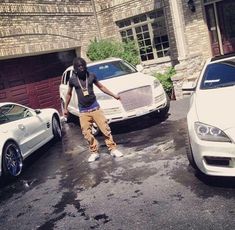 a man standing next to two white cars in front of a brick building with garage doors