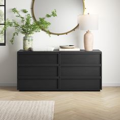 a black dresser with a round mirror on the wall above it and a plant next to it