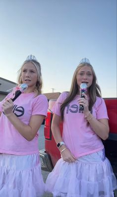 two girls in pink shirts and tulle skirts holding microphones while standing next to each other