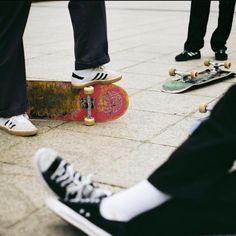 three skateboarders are standing on the sidewalk with their feet propped against each other