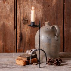 a candle is sitting on a stand next to an old book and a stone jug