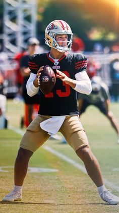 a young man holding a football on top of a field with other people in the background