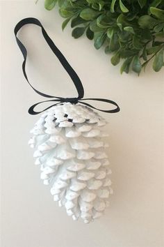 a white pine cone ornament hanging from a black ribbon on a white wall