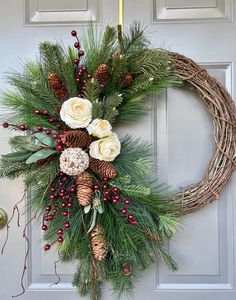 a wreath with flowers and pine cones hanging on a door