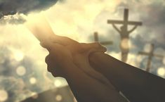 two hands holding each other in front of a cross and sky with sun rays coming through the clouds