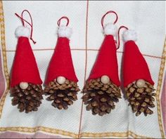 three pine cones with red hats are on a white table cloth and one is hanging from the side