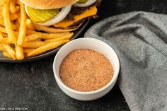 a hamburger and french fries on a plate next to a bowl of seasoning sitting on a table