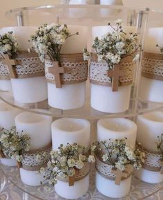 white candles with lace and flowers in them on a glass tray, ready to be used as centerpieces