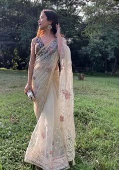 a woman in a white sari is standing on the grass and talking on her cell phone