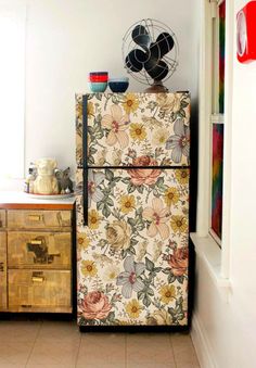 an old fashioned refrigerator is covered in floral fabric and sits next to a cabinet with drawers