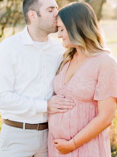 a pregnant couple kissing while standing next to each other