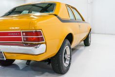 the rear end of an old yellow car in a white garage with no one on it