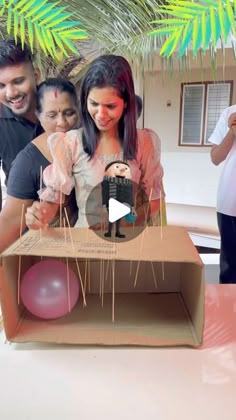 a man and woman holding a baby in a cardboard box with balloons on the table