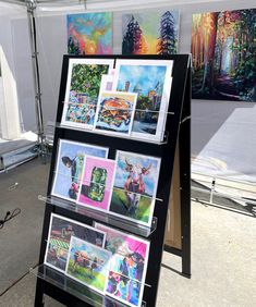 several paintings are on display at an art show in a tent with tables and chairs