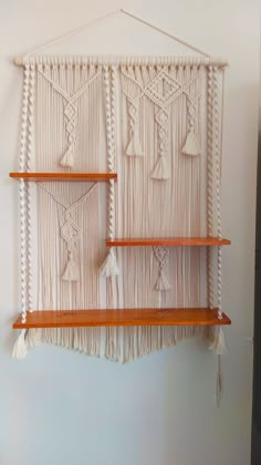 the wall hanging is made with macrame yarn and tasseled wood shelves