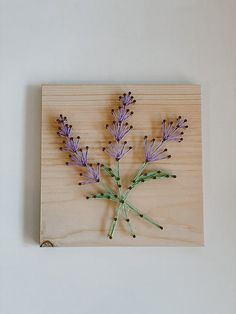 purple flowers are arranged on a wooden plaque with string attached to it, against a white wall