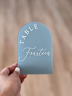 a person holding up a small blue table sign with the word table written on it