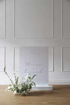 a vase with white flowers sitting on top of a wooden floor next to a sign