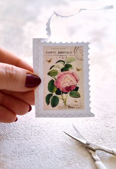 a stamp with a rose on it being held by a woman's hand next to scissors