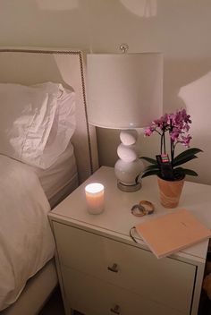 a nightstand with a flower and a candle on it next to a bed in a bedroom