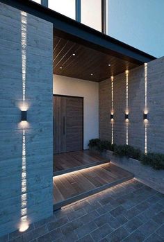 a modern house with lights on the outside wall and wood flooring in front of it