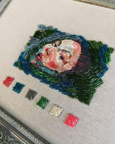 a close up of a cross stitch on a piece of cloth with beads and buttons